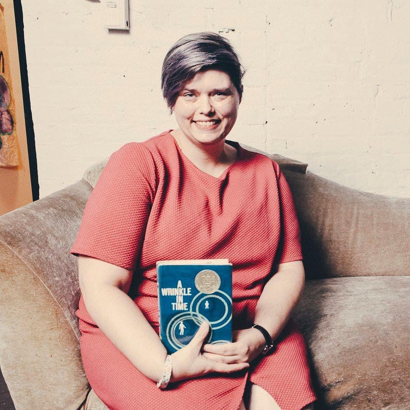 Julie sitting on a chair, holding a copy of the book A Wrinkle In Time.